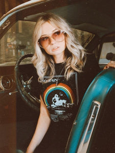 Woman sitting in blue vintage car wearing black seventies style vintage look graphic t shirt with album cover appearance