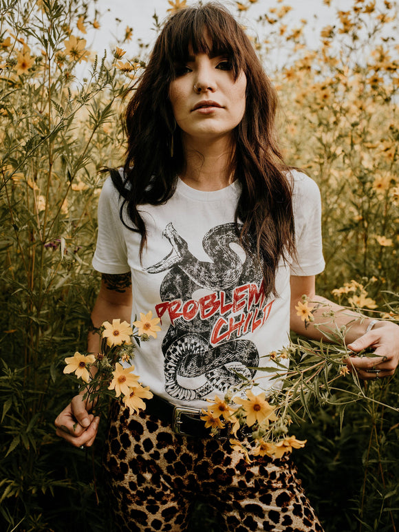 woman wearing problem child grahic tee with snake standing in field of flowers